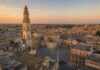 Illustrazione realistica generata con intelligenza artificiale della Piazza del Duomo di Lecce al tramonto, con la Cattedrale e il campanile in stile barocco.
