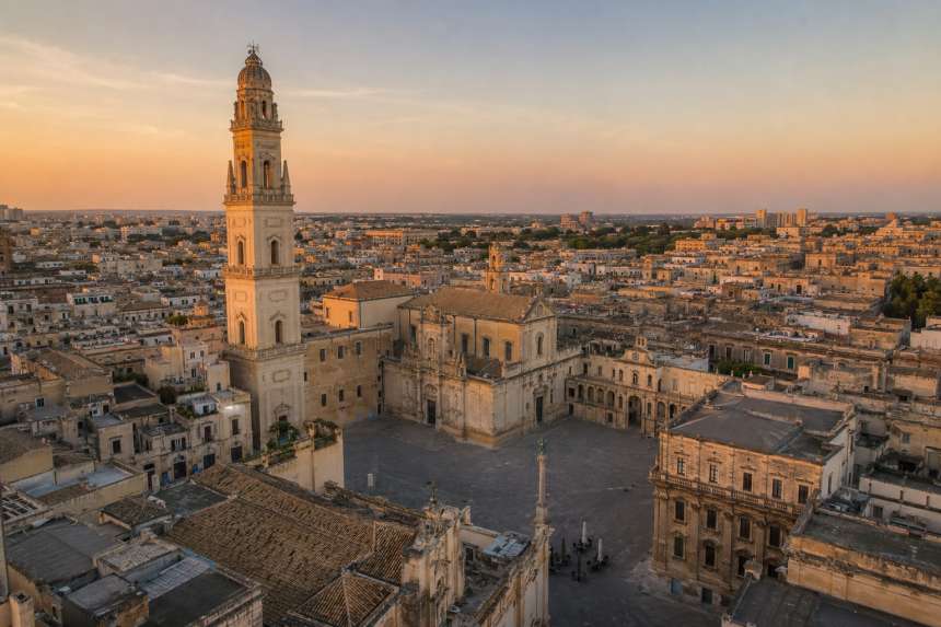 Illustrazione realistica generata con intelligenza artificiale della Piazza del Duomo di Lecce al tramonto, con la Cattedrale e il campanile in stile barocco.